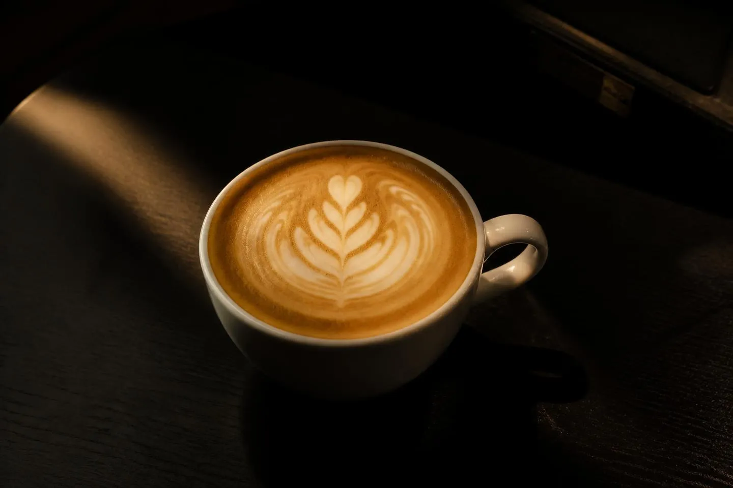 Latte art in a cup lit by a single warm light